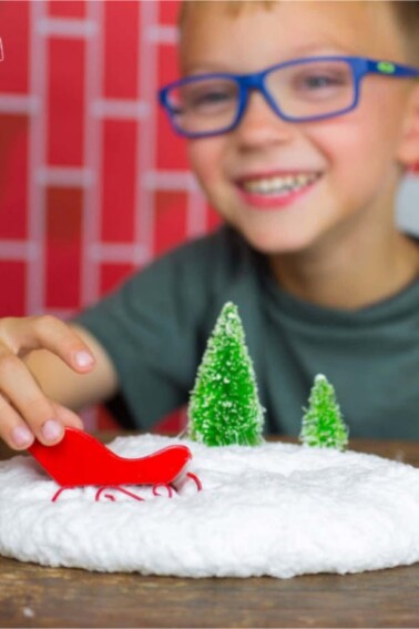 Fluffy Snow Slime Recipe for Kids Winter Activity - Child playing with fluffy snow slime and a mini toy sleigh - Kids Activities Blog