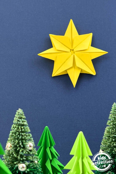 origami star on a dark blue background above origami and ornamental christmas trees