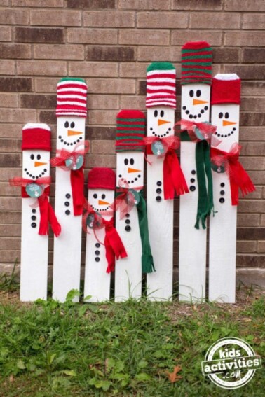 Wooden snowman craft for kids - fence post snowman made of wood shown lined up along wall